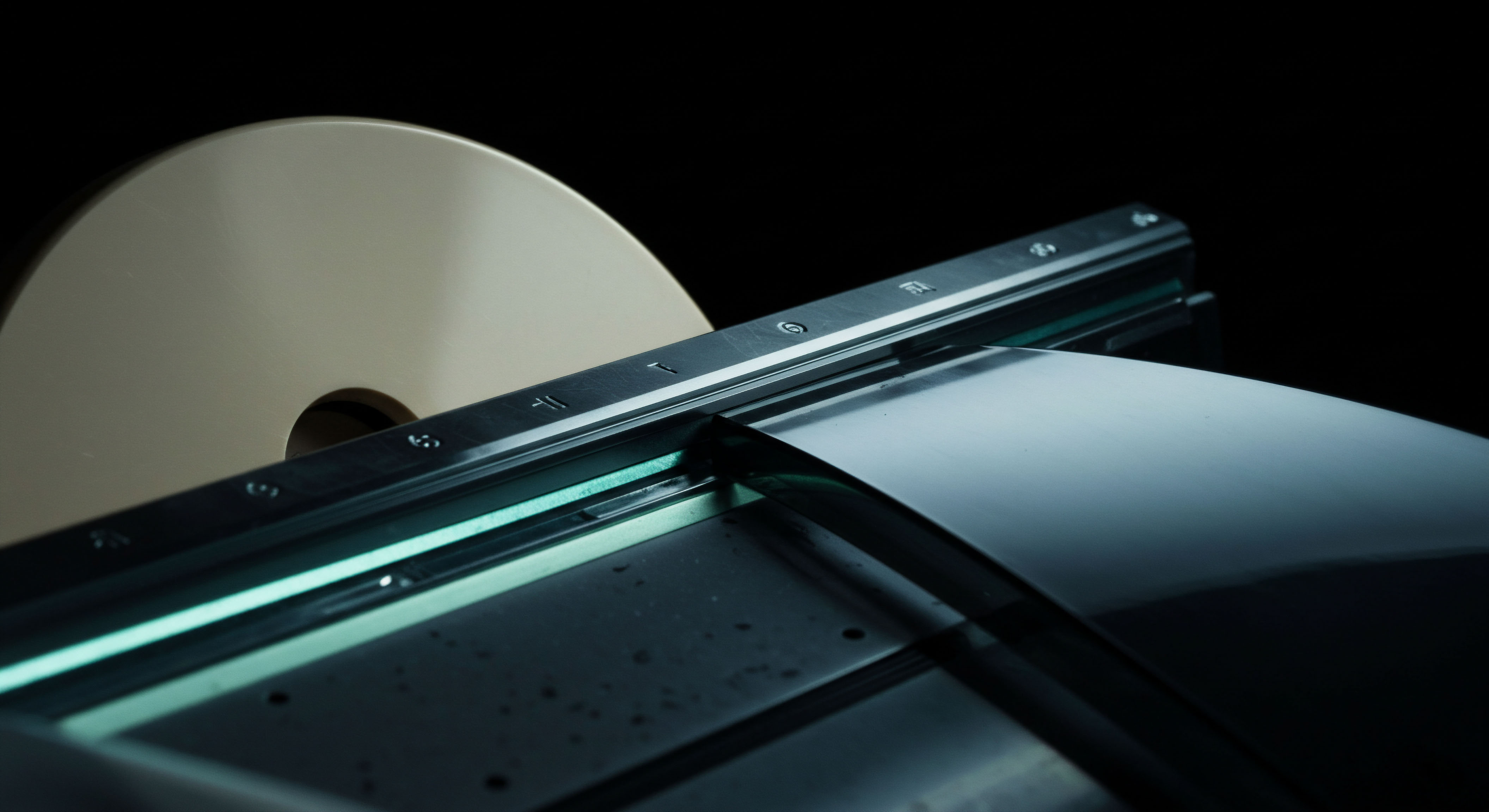 This visualization captures the seamless transition of a large substrate material, suggestive of underlying collateral or ledger tape, moving past an illuminated guidance rail marked with subtle index indicators. The beige, large circular form receding into the background symbolizes a substantial pool of locked assets or staked principal, akin to a centralized high capacity data spool for blockchain verification. The intense teal luminescence underscores a critical processing juncture, perhaps representing the real time settlement or execution of complex exotic options strategies deployed within decentralized finance DeFi protocols. Key concepts manifest as perpetual swap funding rates maintenance, automated tiering of staking rewards, hash rate allocation stability, and transparent on chain derivative contract instantiation, illustrating the industrialized infrastructure supporting scalable digital asset custody and high frequency trading execution flows.