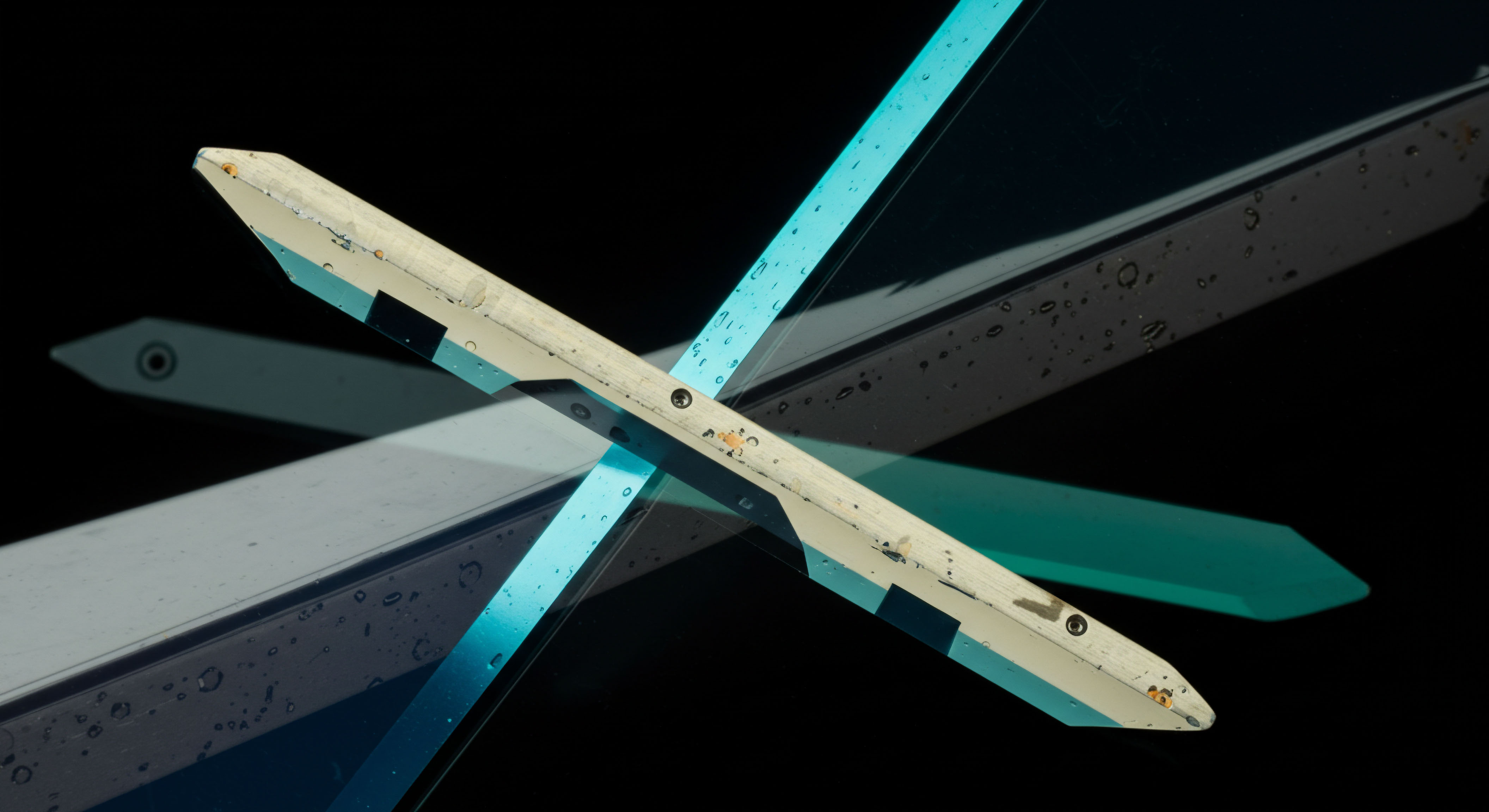 This abstract composition features two aged, off-white structural elements intersecting against absolute blackness, overlaid with translucent cyan light bands exhibiting water droplets, suggesting operational stress. The visual intersection models complex derivatives architecture, specifically reflecting the bifurcation inherent in synthetic asset replication strategies utilized in decentralized finance. The sharp angles and dual overlapping planes symbolize strike price divergence and the need for precise basis risk management within perpetual futures contracts. The reflection, showing a faint target-like marker, hints at calibrated liquidation thresholds necessary for maintaining margin integrity in high-leverage crypto options environments, navigating market metastability.