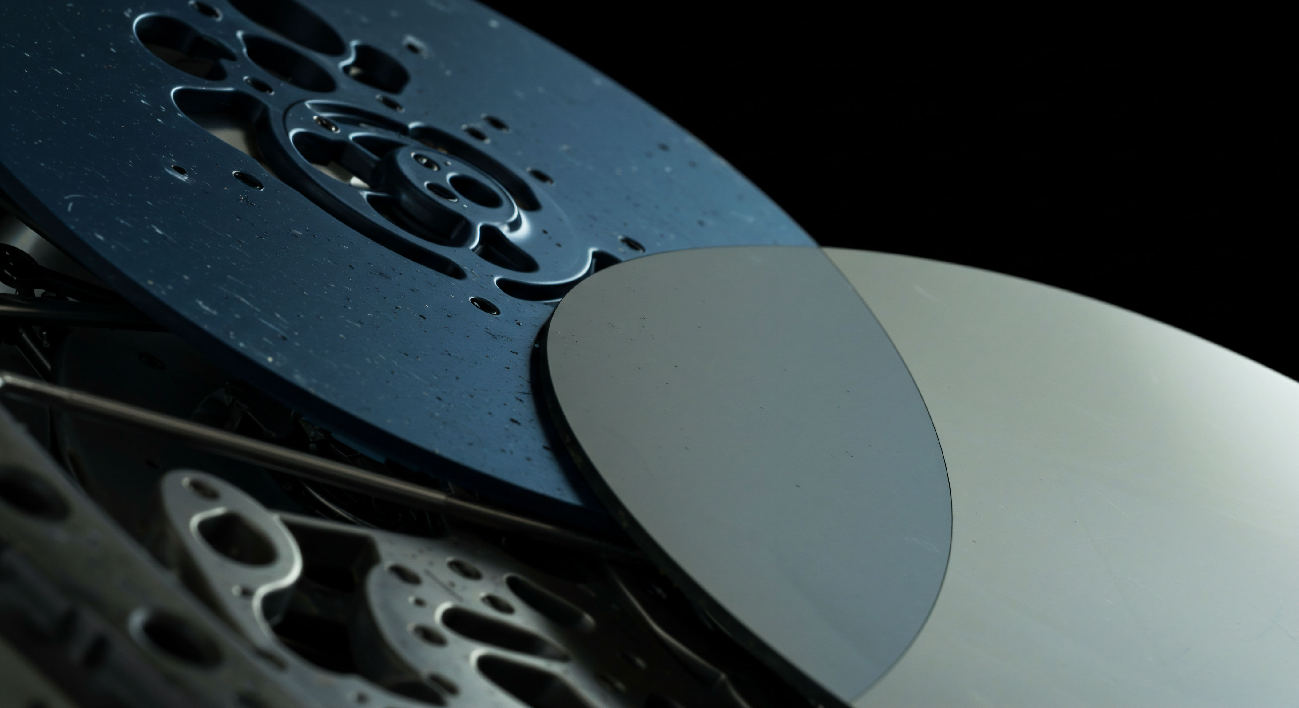 Reflective semiconductor wafers overlap a dark, intricately perforated metallic component suggesting micro-machinery necessary for high-frequency trading infrastructure or hardware wallet validation mechanisms. The juxtaposition symbolizes the confluence of physical state security, or tangible collateralization underpinning digital asset exchange. This structure evokes concepts of base layer settlement layers or the physical security required for custody solutions like cold storage entropy generation, crucial for managing off chain ledger state security protocols. Terms like slippage minimization, collateralization ratios, and atomic swaps manifest in this material juxtaposition. The smooth reflective plane hints at pristine data integrity requisite for transparent on chain governance models and secure private key derivation across decentralized autonomous organizations utilizing complex derivatives strategies.