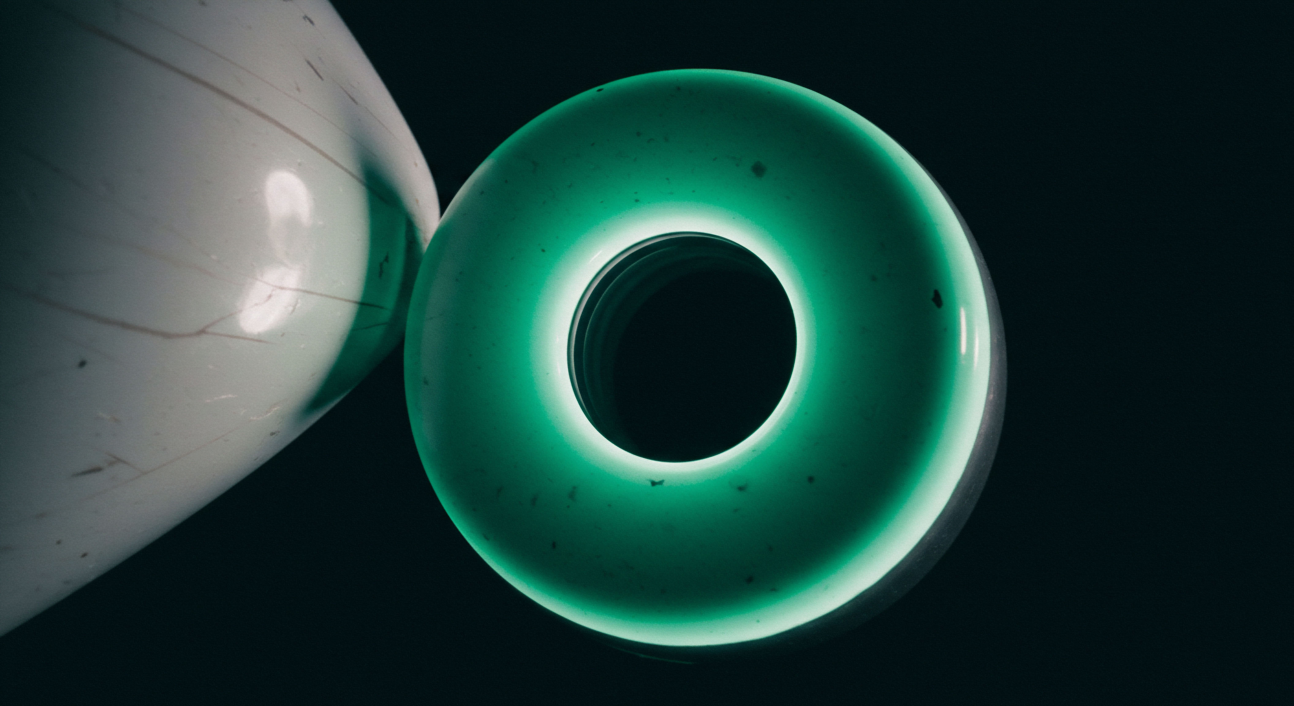 This visualization captures a sharply focused, internally illuminated emerald torus juxtaposed against a matte off-white cylindrical form against deep matte blackness. The radiant green aperture suggests a perpetual motion mechanism, potentially representing high-frequency algorithmic trading or smart contract execution flow. The torus emits a vivid Gaussian blur boundary, akin to liquidity provision in decentralized finance protocols or the implied volatility surface of exotic options. Keywords like Gamma exposure, perpetual swaps settlement, collateralized debt positions CDP, dark pool liquidity aggregation, and Black Scholes modeling adjustments are invoked by this abstract representation of market dynamics. The composition symbolizes the complex interplay between intrinsic value decay and extrinsic premium valuation in derivative contracts, perhaps illustrating the geometric structure of an options moneyness gradient across time horizons.