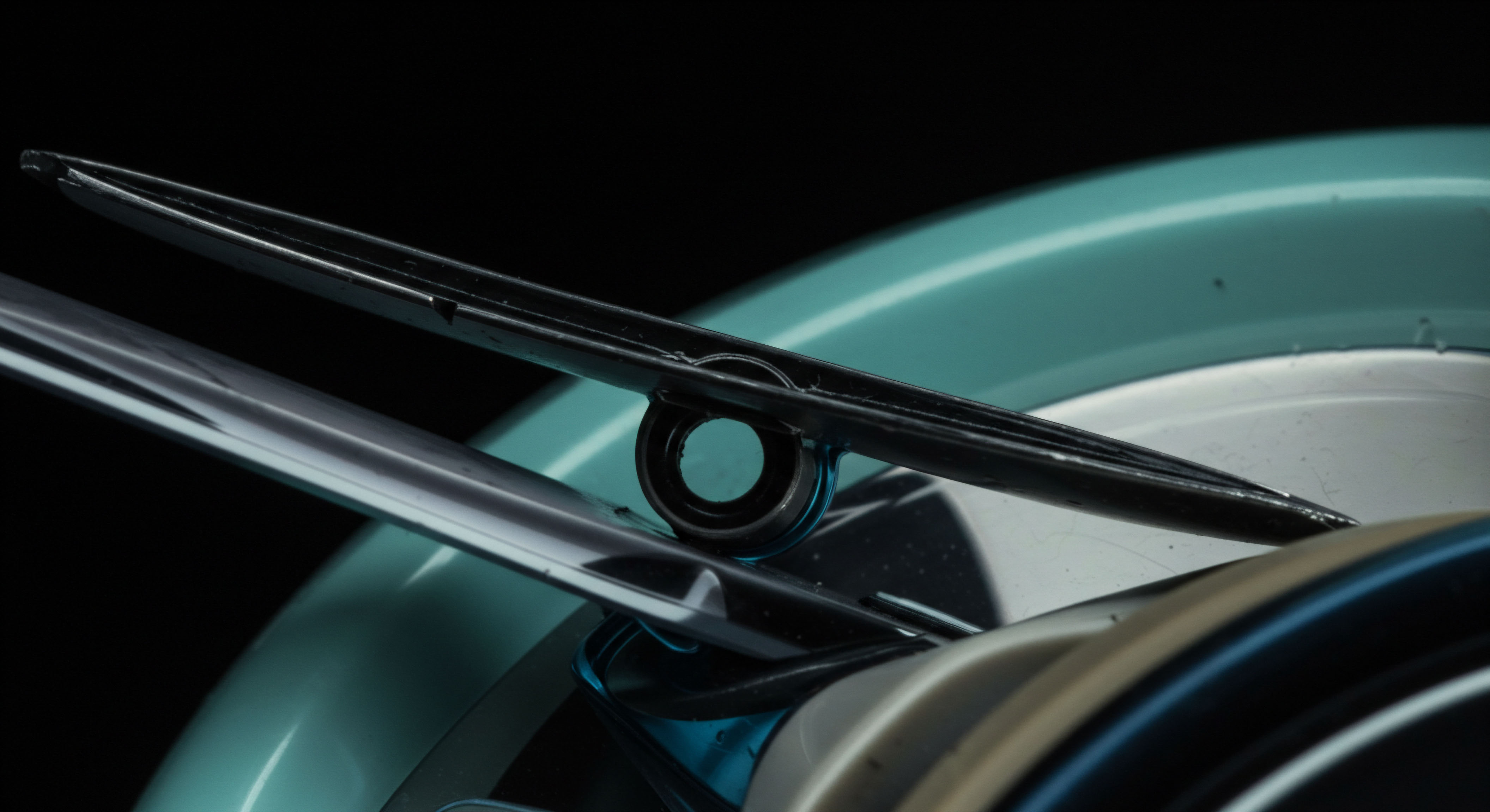 This stark close-up isolates two metallic structures crossing over a smooth teal surface suggesting underlying network architecture. The upper component, dark and linear, pierces a central nodal point represented by a small ring, mimicking the precise execution of an options contract strike price validation. The lower reflective element symbolizes rapid capital flow or high-frequency settlement across decentralized finance rails. This juxtaposition illustrates the delicate, mechanical interplay required for secure margin maintenance and immutable ledger reconciliation in complex perpetual futures or volatility index derivatives trading protocols where slippage tolerance is negligible for alpha capture. Focus rests on the precise leverage mechanism governing synthetic asset exposure relative to spot market dynamics.