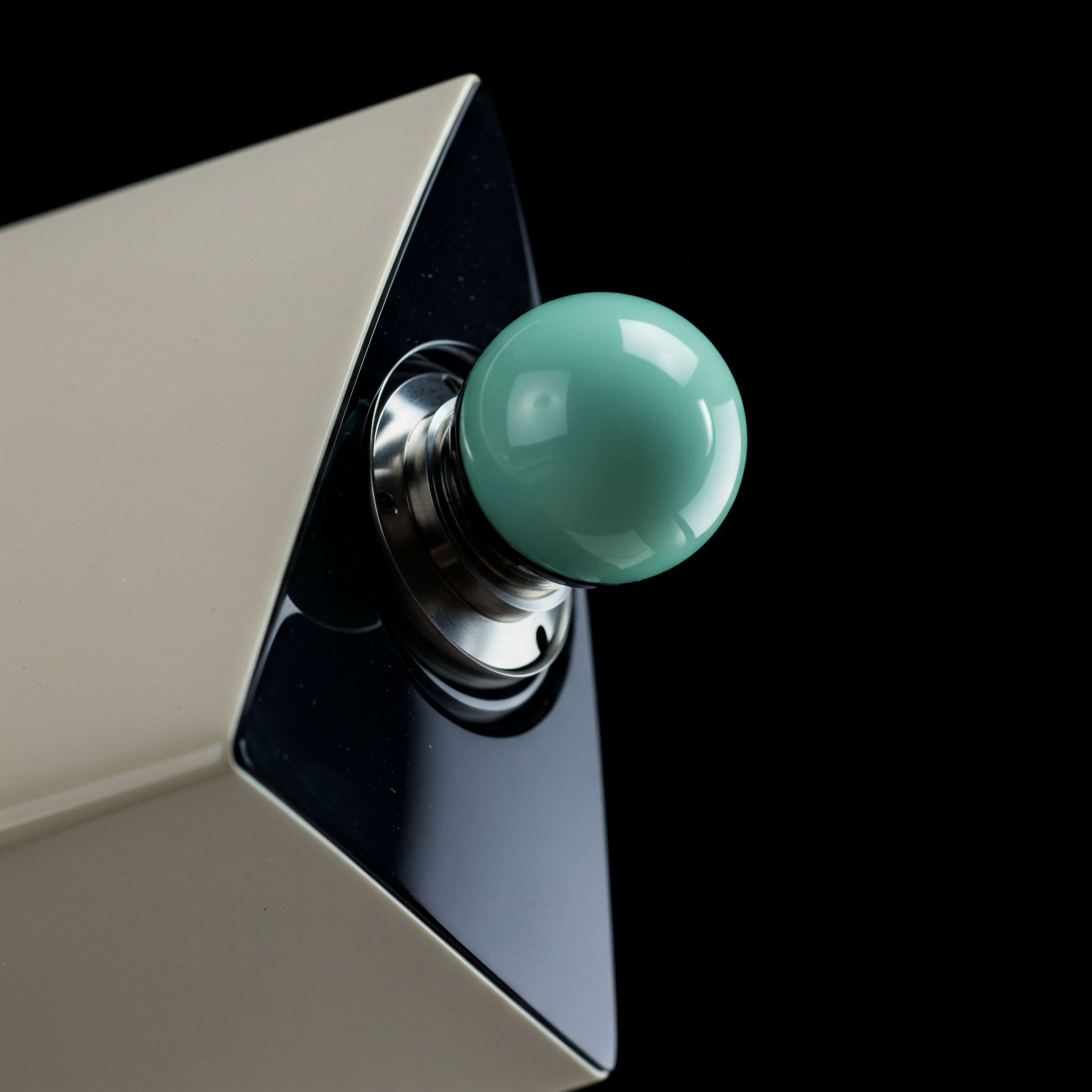 This close-up captures a high-gloss, seafoam green spherical actuator mounted on a brushed metal gimbal set against an angled housing featuring beige plating and deep black reflective facets. The composition symbolizes the tactile interface within sophisticated algorithmic trading systems, perhaps representing a joystick controller for manual override of automated market making protocols. The smooth sphere evokes the delicate equilibrium required for successful options pricing volatility skew management. It suggests the precision needed for executing atomic unit swaps or managing perpetual futures positions within a highly capitalized decentralized finance environment, balancing gamma exposure against vega risk in decentralized exchange environments.
