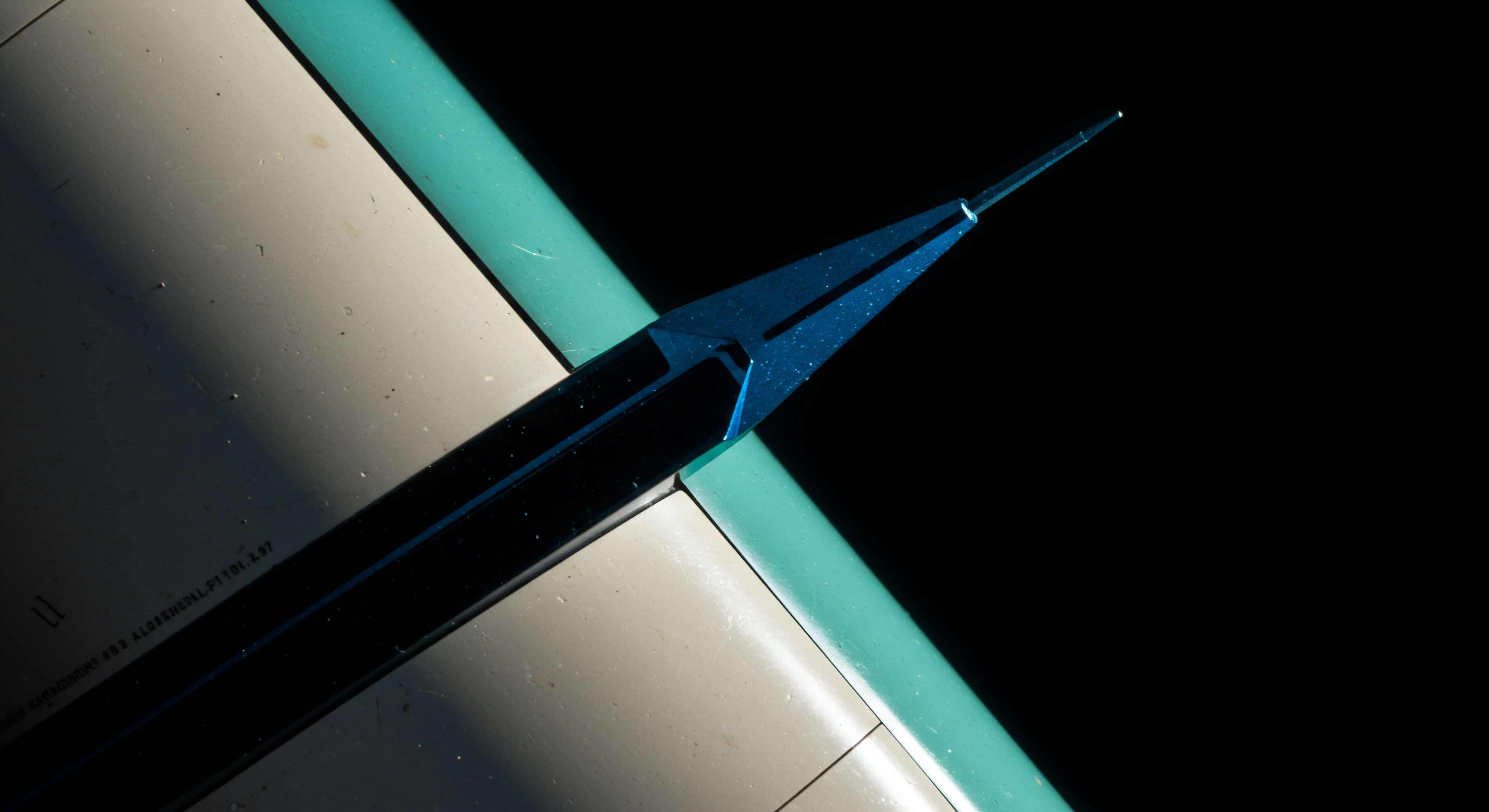 This macro view captures a highly reflective, sharp blue metallic point intersecting a muted beige planar surface, bordered by a contrasting teal edge, symbolizing the razor-thin margin of execution in financial engineering. The intense directional lighting emphasizes specular highlights, analogous to real-time data flows hitting a trading algorithm executing complex derivative strategies. The structure suggests a delta-hedging needle or a specialized probe for validating DeFi smart contract endpoints, referencing the precise strike price determination in options contracts. Key nomenclature involves understanding synthetic positions derived from underlying blockchain assets, where liquidity fragmentation impacts slippage in atomic swaps and the geometry echoes candlestick formations revealing imminent volatility clustering within perpetual futures markets. The dark background isolates the action mirroring opaque order book depth in an RFQ system.